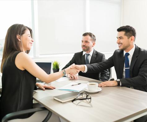 Confident female leader welcoming male employees with a handshake in office